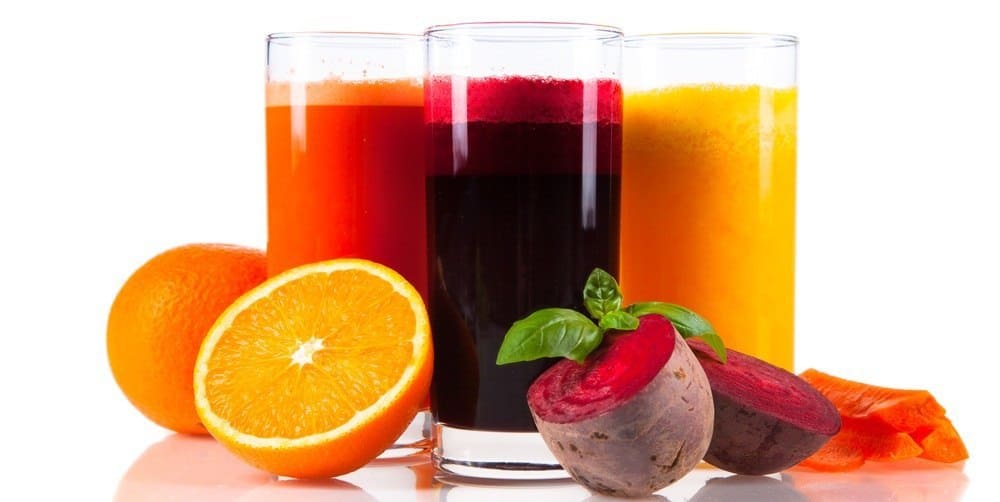 Three glasses of fruit juice with various fruits and vegetables next to them.
