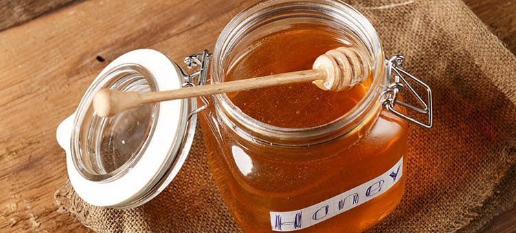 An open jar of honey with a sticker titled 'honey' and a honey dipper placed inside.