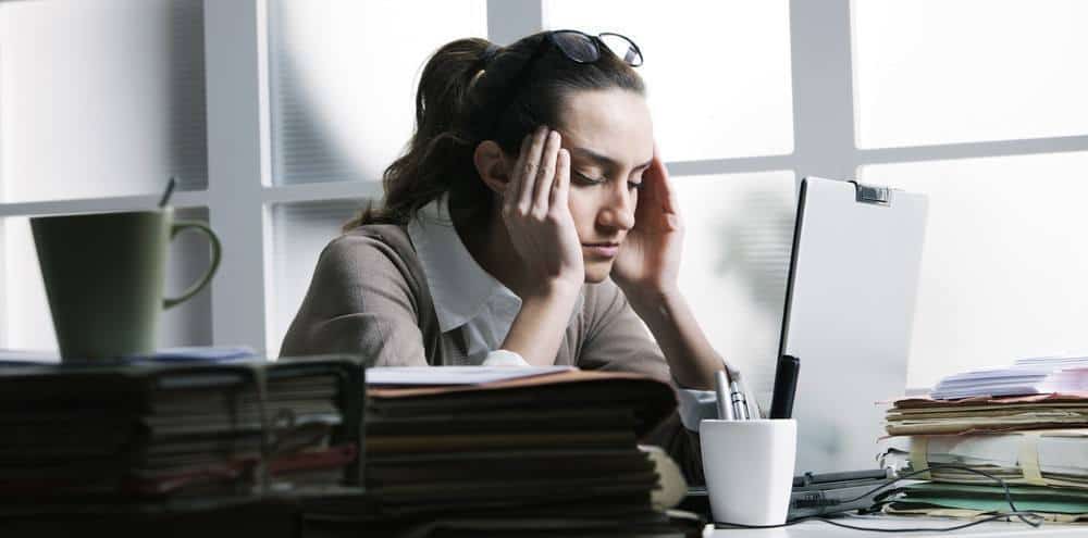 A woman sitting at an office table with a noticeable migraine.