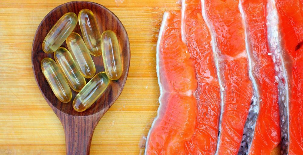 Fish oil capsules in a spoon next to slices of fish.
