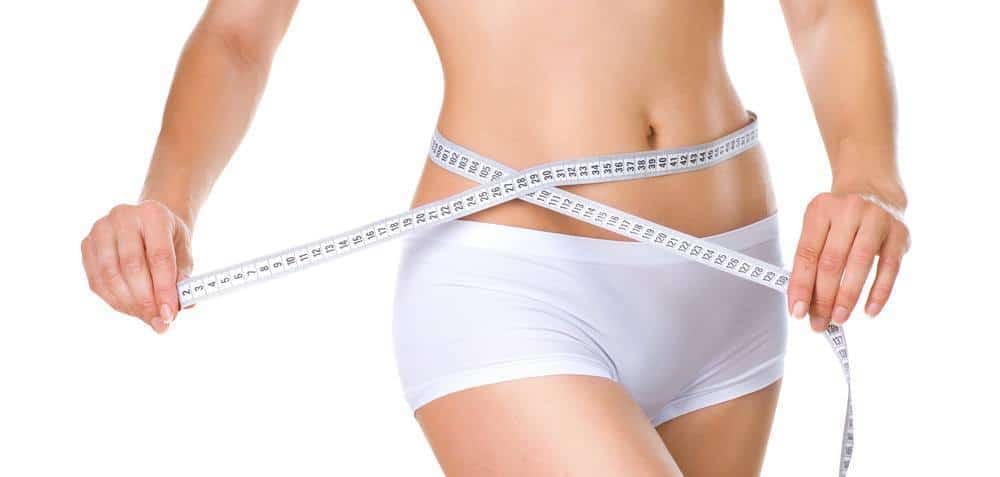 Image of the lower body of a woman measuring her waistline with tape.