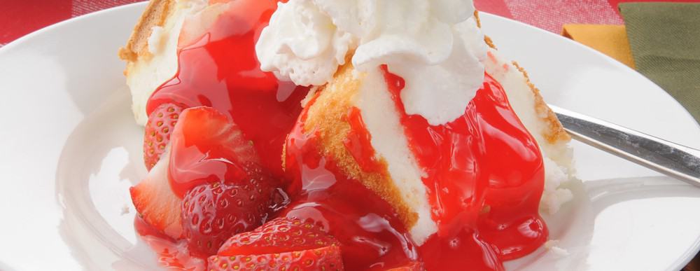 A slice of strawberry shortcake presented on a plate with cream.
