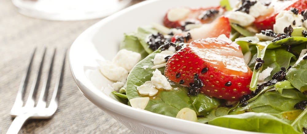 A plate of salad with various greens and a strawberry.