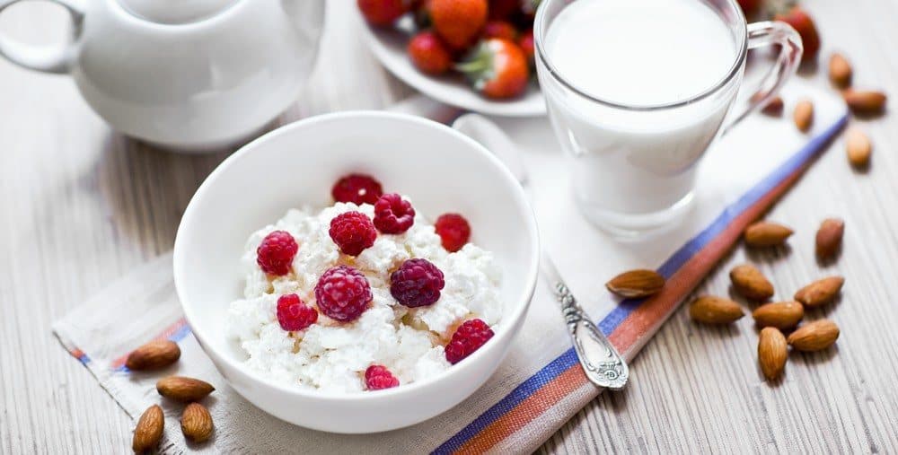 A bowl of cottage cheese topped with raspberries, next to a glass of milk.