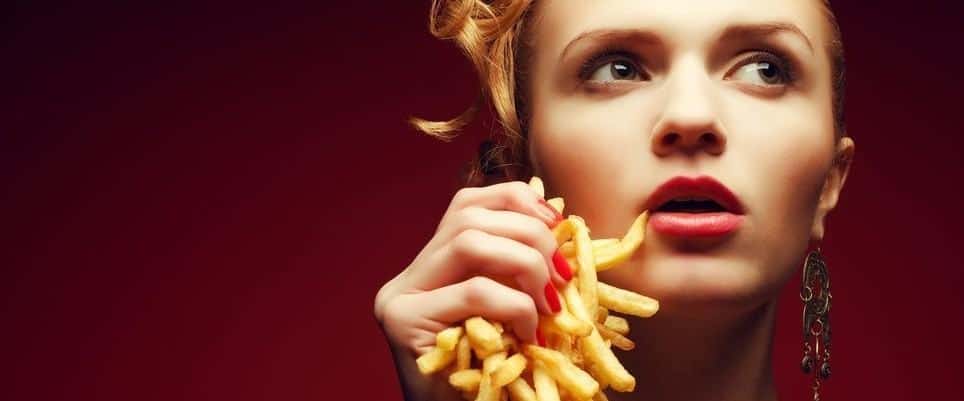 A stylish woman holding a handful of french fries in front of a red background.