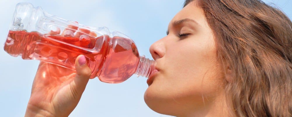 A woman drinking a faintly red sugary drink from a plastic bottle.