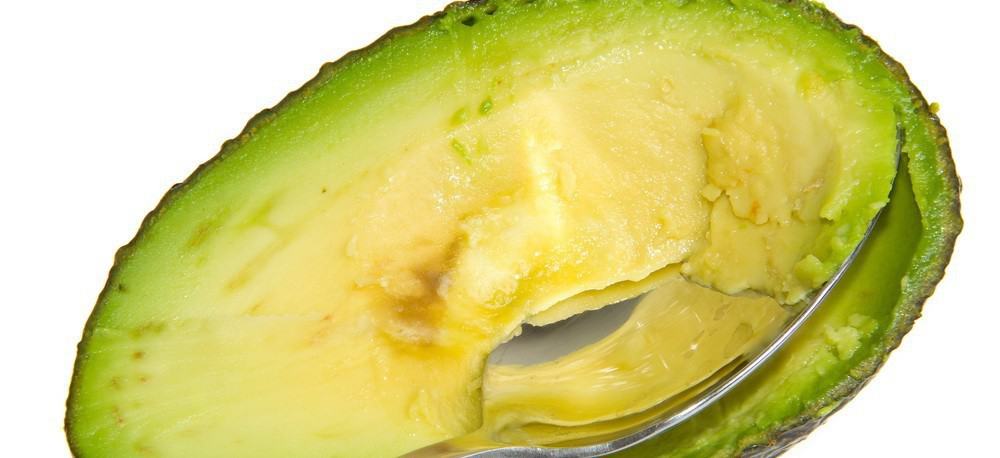 A spoon being used to scrape the inside of an avocado.