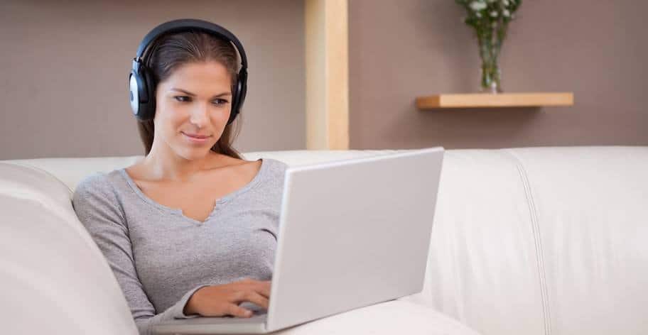A woman sitting on a couch with her laptop with headphones on.