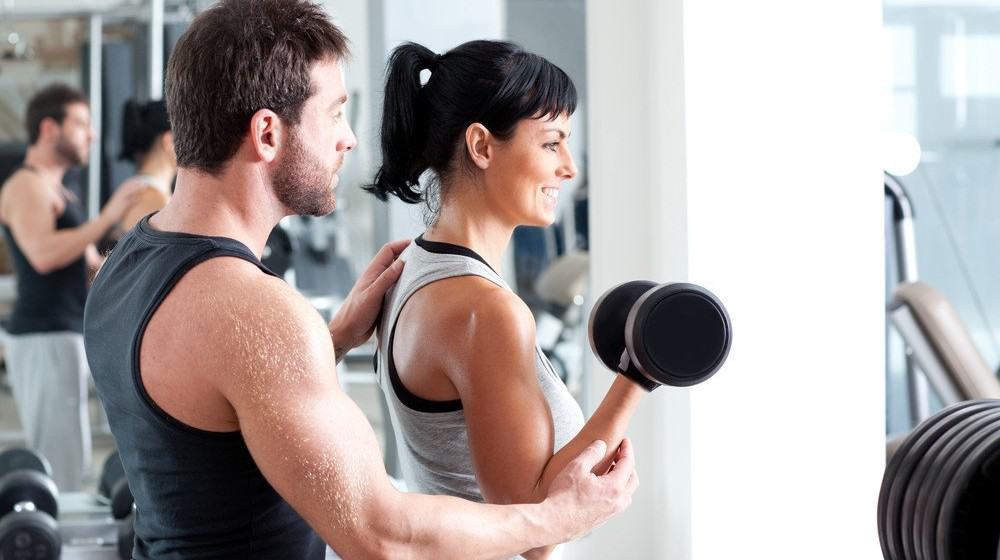 A trainer helping a woman with a dumbbell exercise.