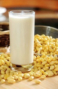 A glass of soy milk with a bunch of soy beans around it.