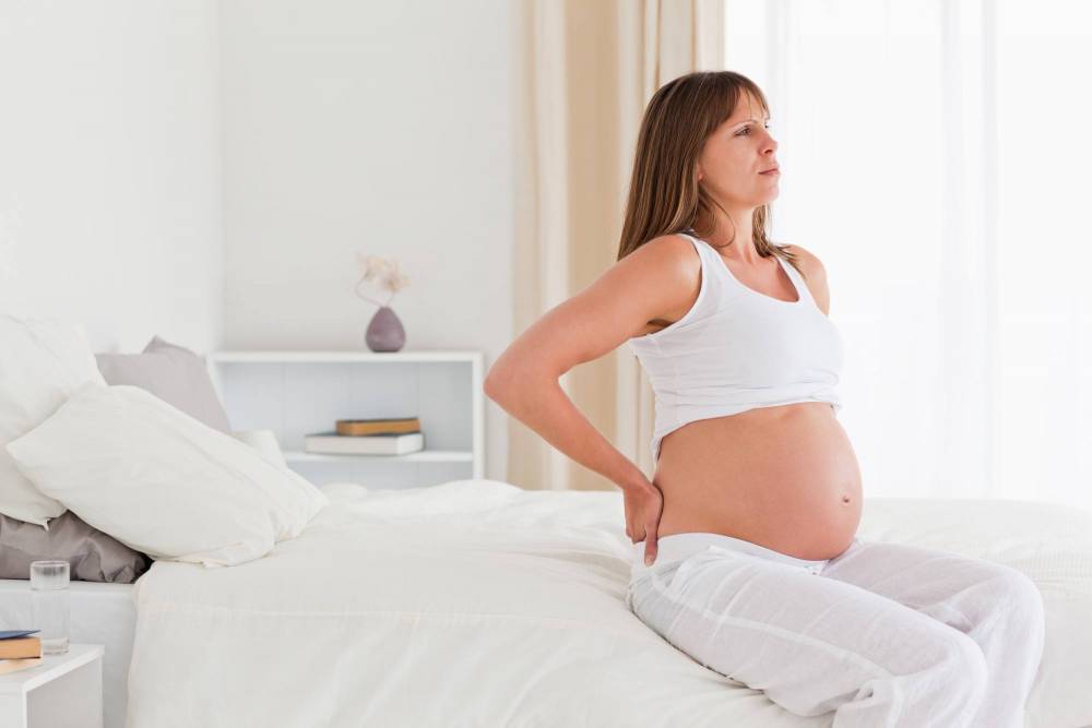A pregnant woman with back pain sitting at her bed.