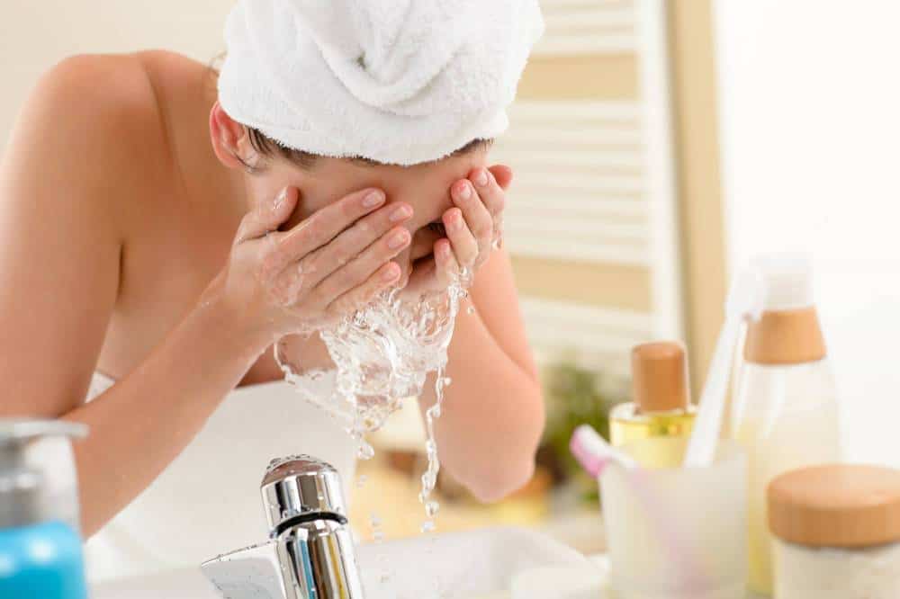 A woman cleaning her face at the sink.