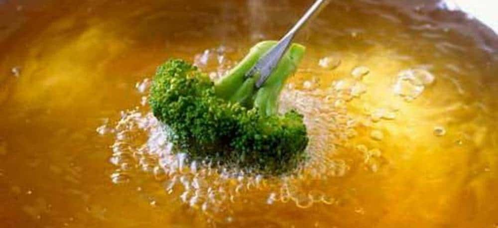 Broccoli being put into a large pot of boiling oil.