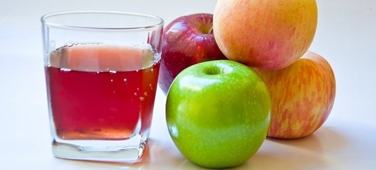 A glass of apple juice next to some apples.