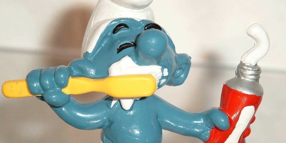 A smurf statue brushing teeth and holding a tube of toothpaste.