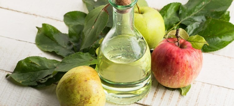A glass of apple cider vinegar surrounded by apples.
