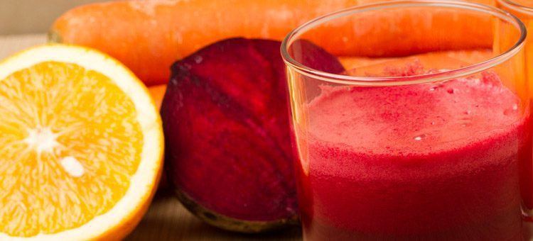 A glass of beet juice with an orange and a carrot.