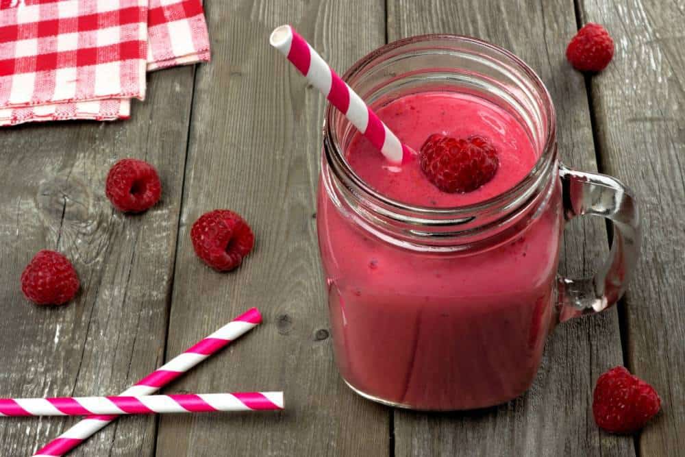 A large glass of pink raspberry smoothie with straws.