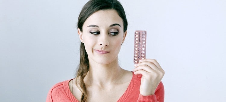 A young woman looking at birth control pills with suspicion.