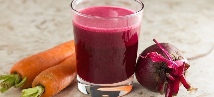 A glass of carrot beet juice next to a beetroot and carrots.
