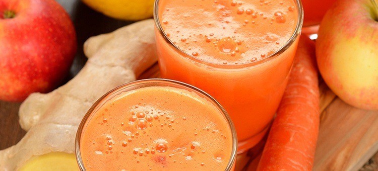 Glasses of carrot-ginger-apple juice with ginger root, apples, and carrots next to them.