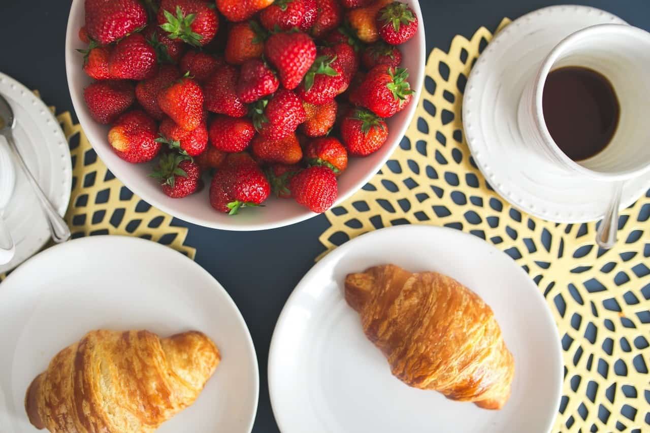 A light breakfast with croissants, a bowl of fruit, and coffee.