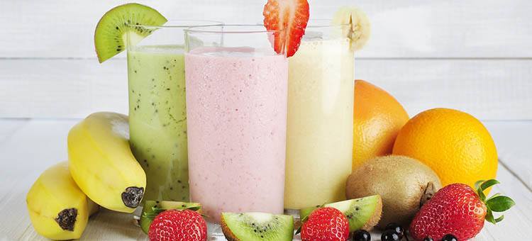 Glasses of various smoothies surrounded by fruit.
