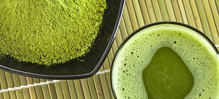 A cup of matcha tea next to a small plate of matcha powder.