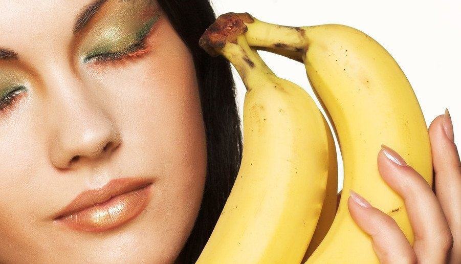 A model holding bananas next to her face.