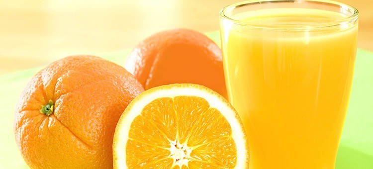 A glass of orange juice next to some oranges.