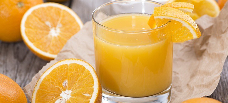 A glass of orange juice next to some oranges.