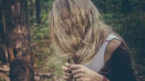 A girl fiddling with split hairs in a forest.