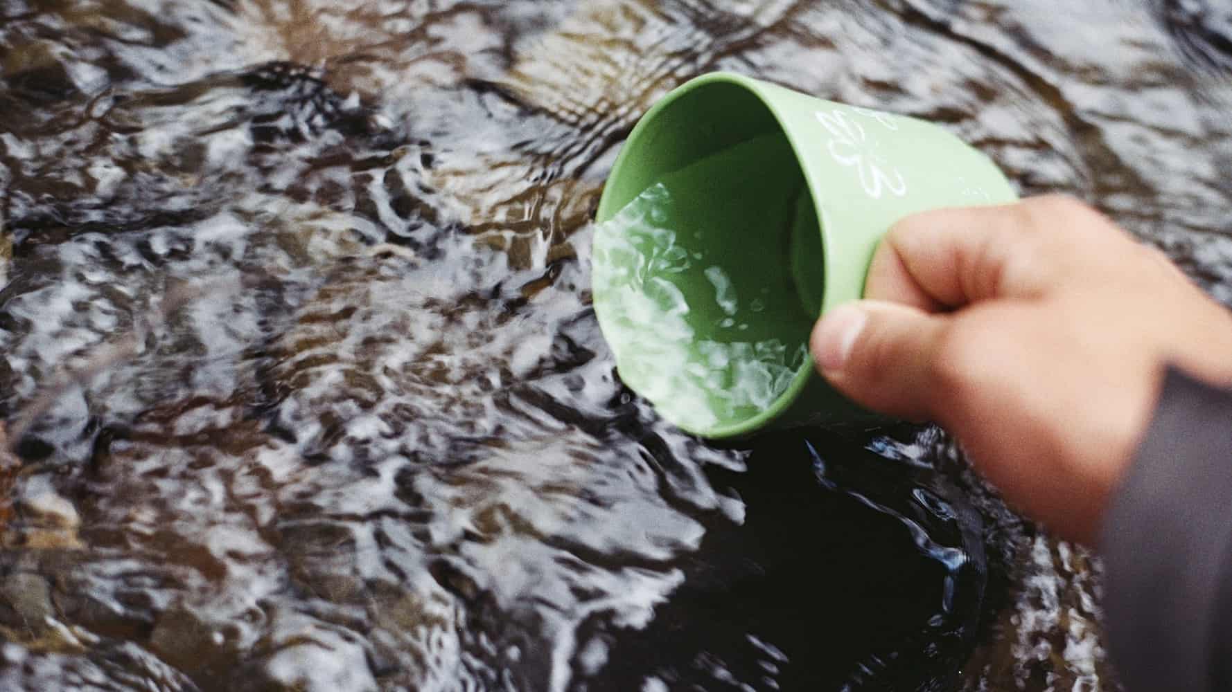 A person using a mug to draw water from a river.