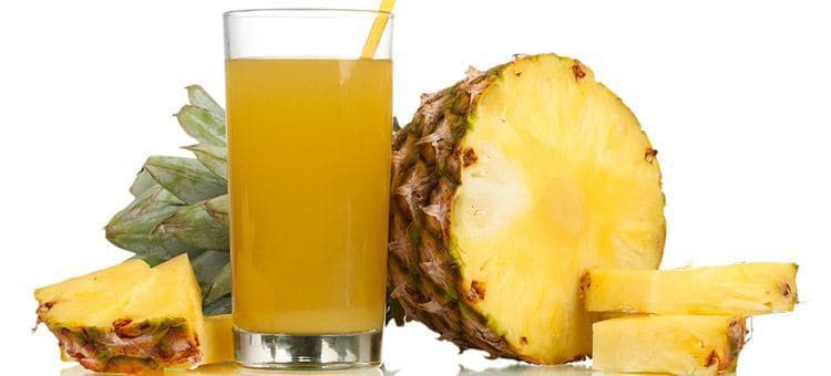 A glass of pineapple juice next to half of a pineapple.