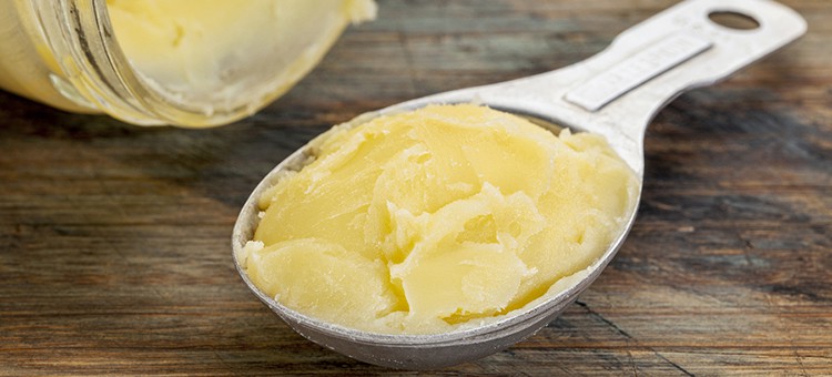 A spoon of raw butter next to a jar of raw butter.