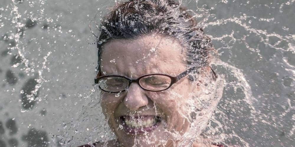 A woman being splashed with in the face with water.
