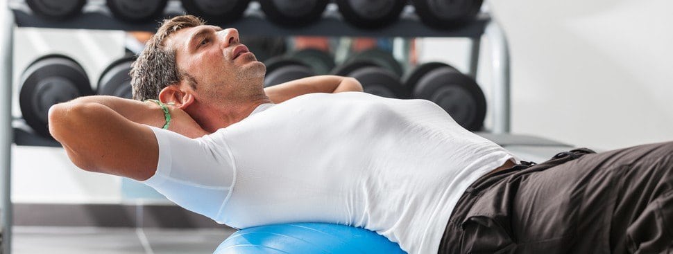 A man doing sit-ups while balancing on a fitness ball.