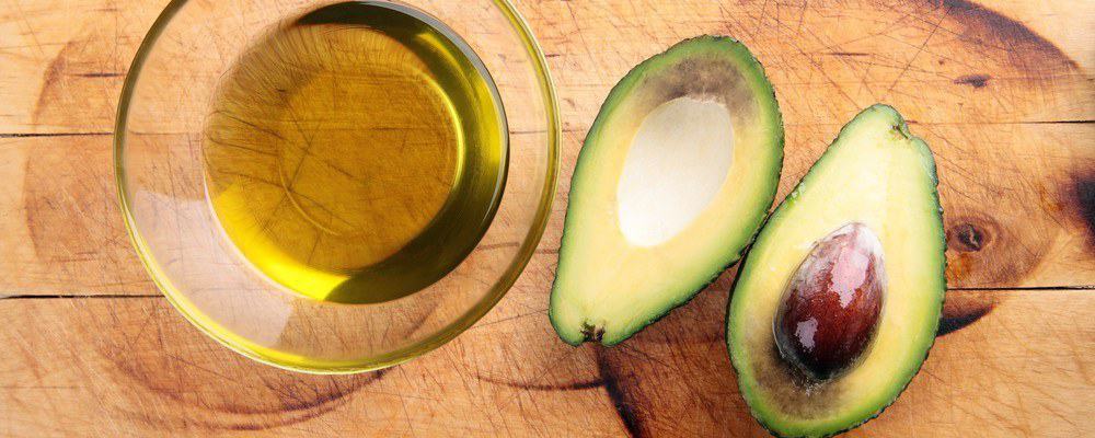A glass of avocado oil and an avocado sliced in two.