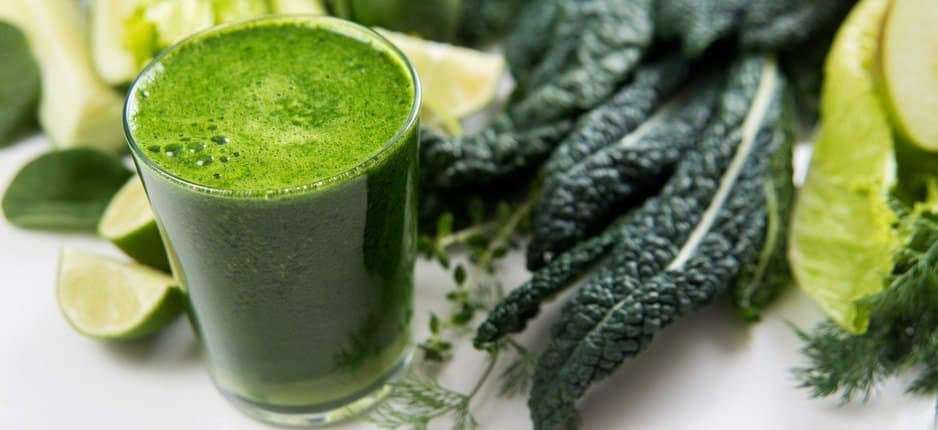 A glass of kale juice next to a batch of kale.