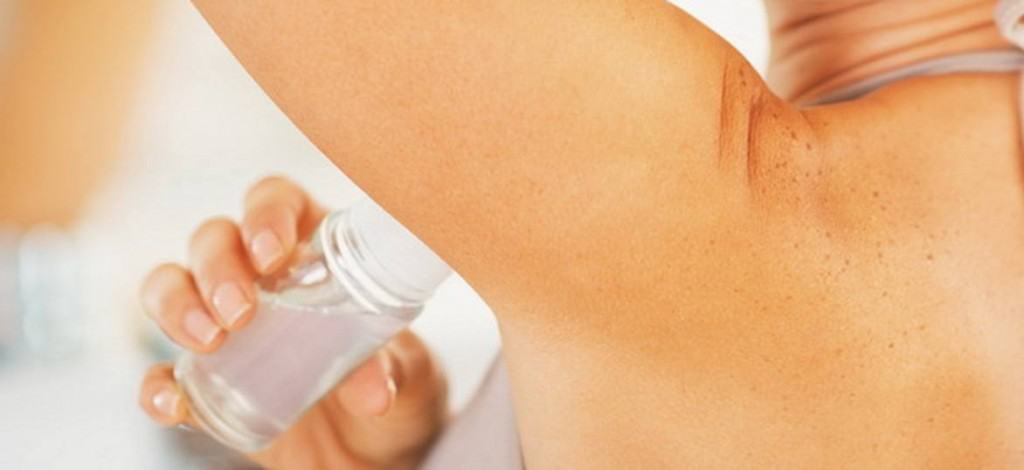 A woman applying deodorant to her armpits.