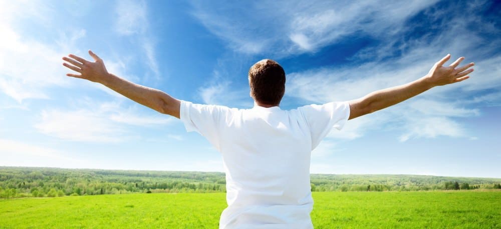 A person cheering at the sky on a beautiful green plain.