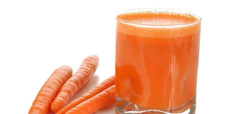 A glass of carrot juice next to carrots.