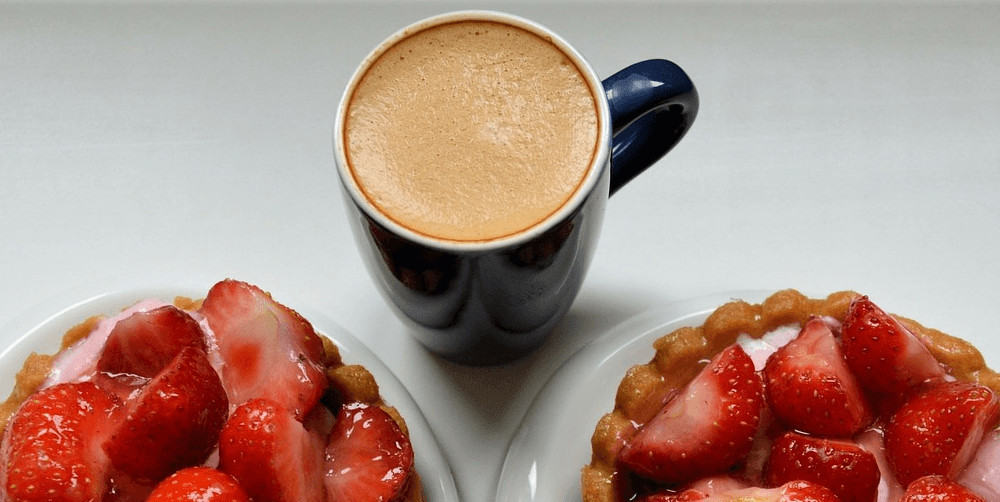 A mug of strawberry coffee with plates of strawberries.