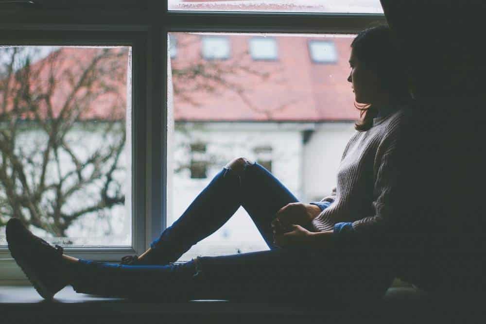 A depressed woman sitting in a window.