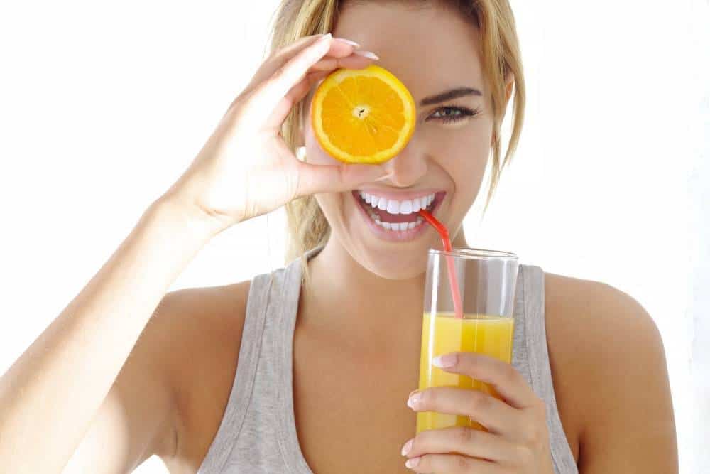 A woman holding a glass of orange juice and an orange to her eye.