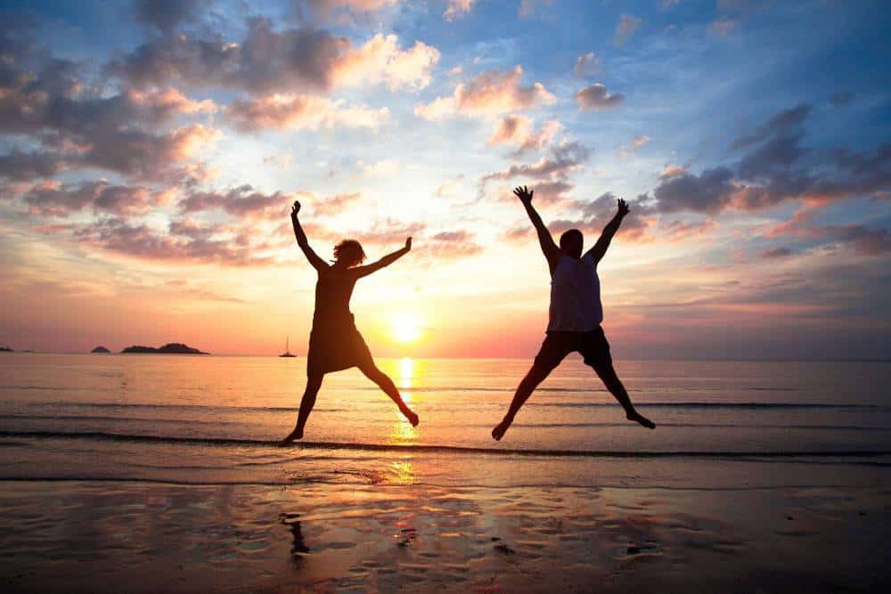 A happy couple jumping on a sandy beach.