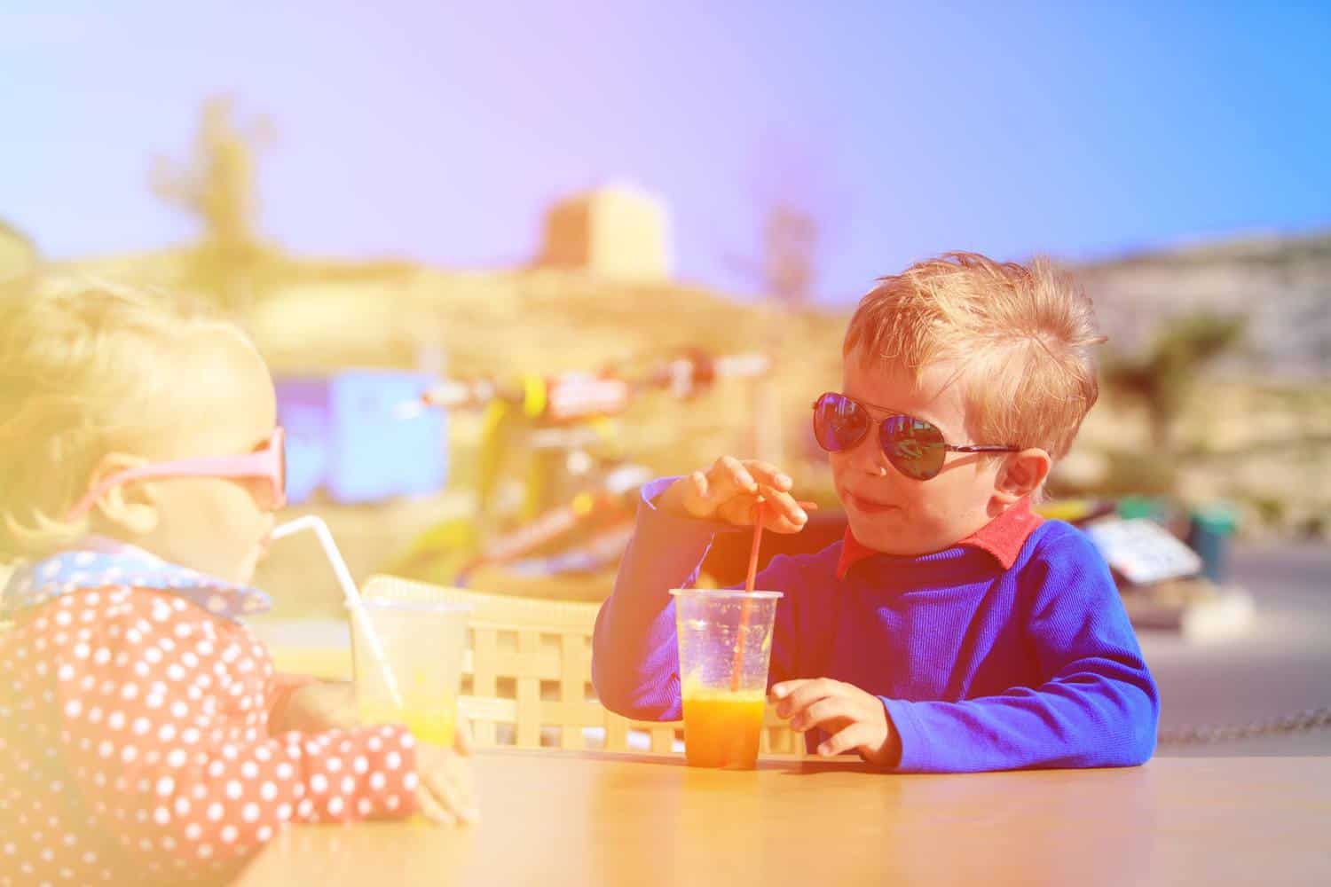 Two young children enjoying drinks at the beach.