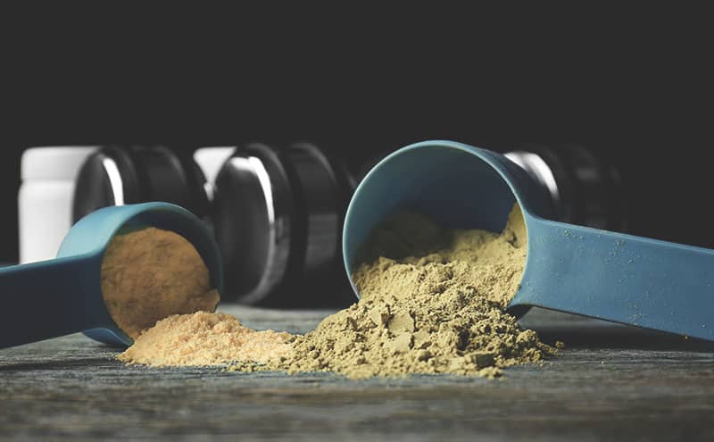 Two scoops of hemp protein powder, in front of dumbbells.