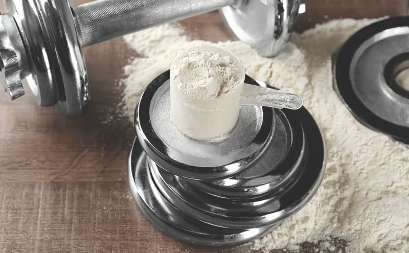 Creatine in a scoop, on weights, next to a dumbbell. 