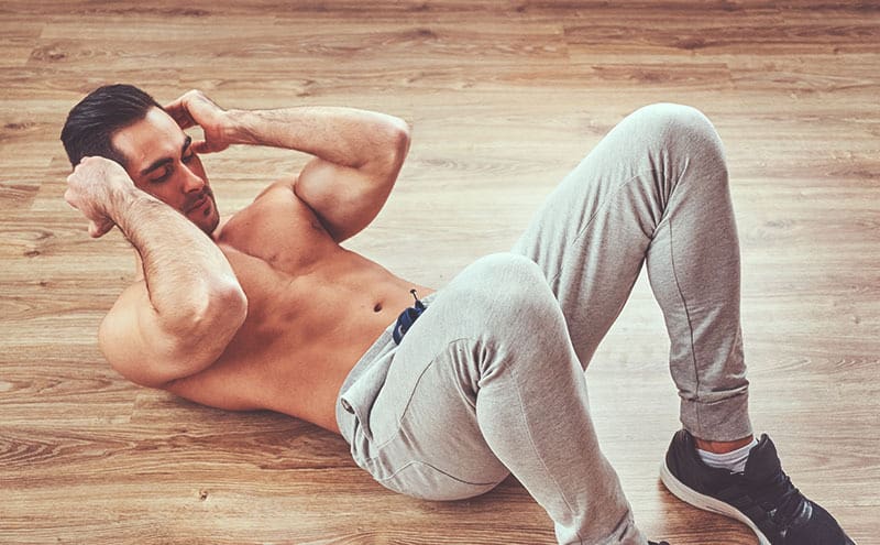 Shirtless man doing sit-ups on wooden floor, after taking one of the best ceatine pills.